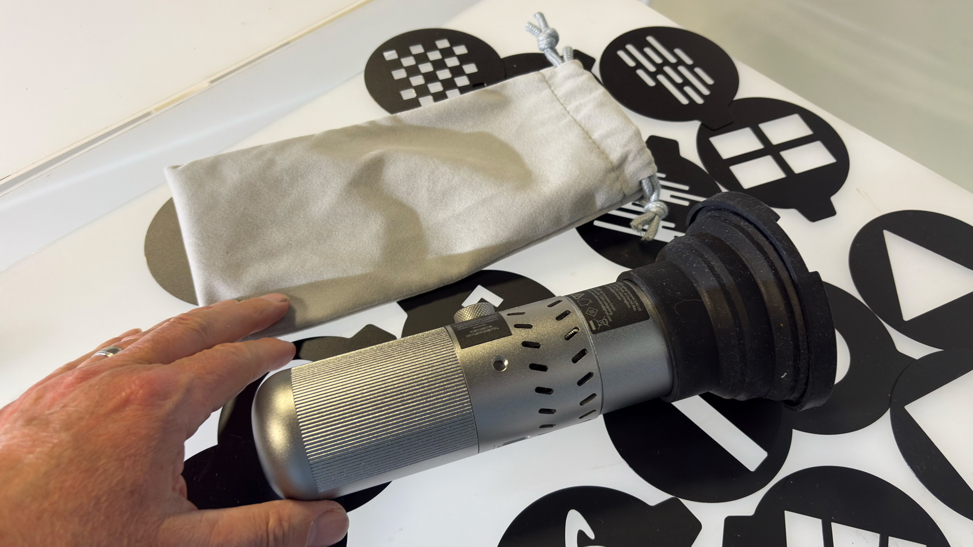 Shot of the Neewer FL20 flashlight lying on a table next to the kit&amp;rsquo;s supplied cloth drawstring bag. The 20 supplied stencils are scattered on the table.