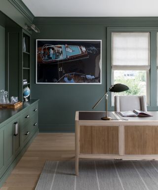 Color drenched green office with wooden desk and lamp