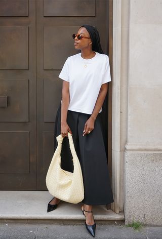 a black maxi skirt outfit showcasing a woman wearing a white t-shirt with a black full-skirt maxi and a yellow woven handbag and black pointed kitten heels