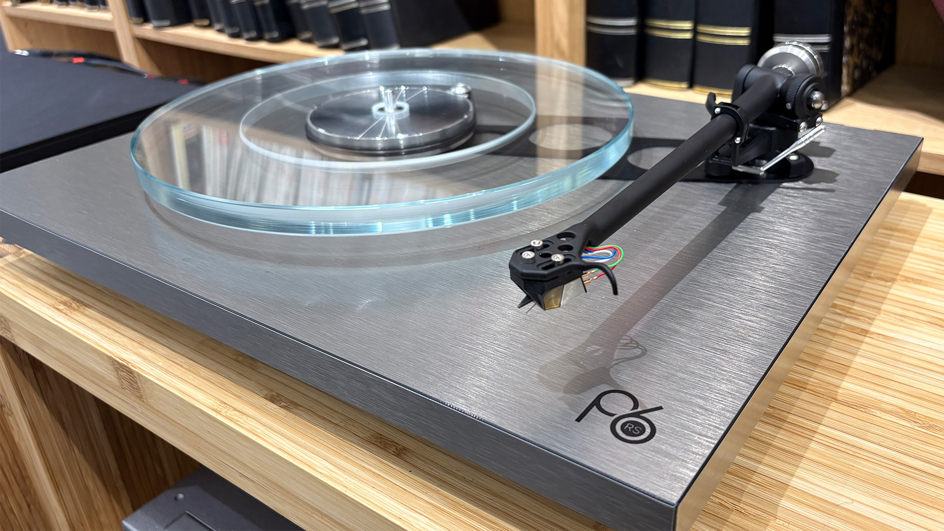 Rega Planar 6 RS Edition turntable on wooden hi-fi rack in front of bookcase showing glass platter