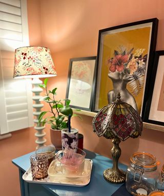 A drop zone in my study showing a blue sideboard in a terracotta colored room with white shutters, lamps, plants and artwork on the wall. The drop zone is a tray with cups and plastic food containers piled up