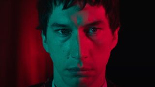 Adam Driver stands stocially as he's bathed in both green and red light in Megalopolis.