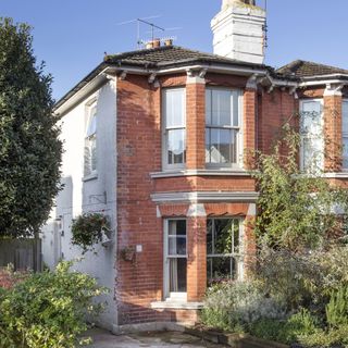 red brick period house exterior with bay windows and white rendered side walls
