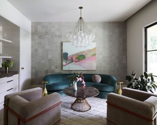 living room with teal curved sofa, neutral armchairs, gray patterned rug, bar and glass globe ceiling pendant