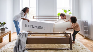 A family of 3 getting a tuft and needle mattress out of a box to use on a bed frame