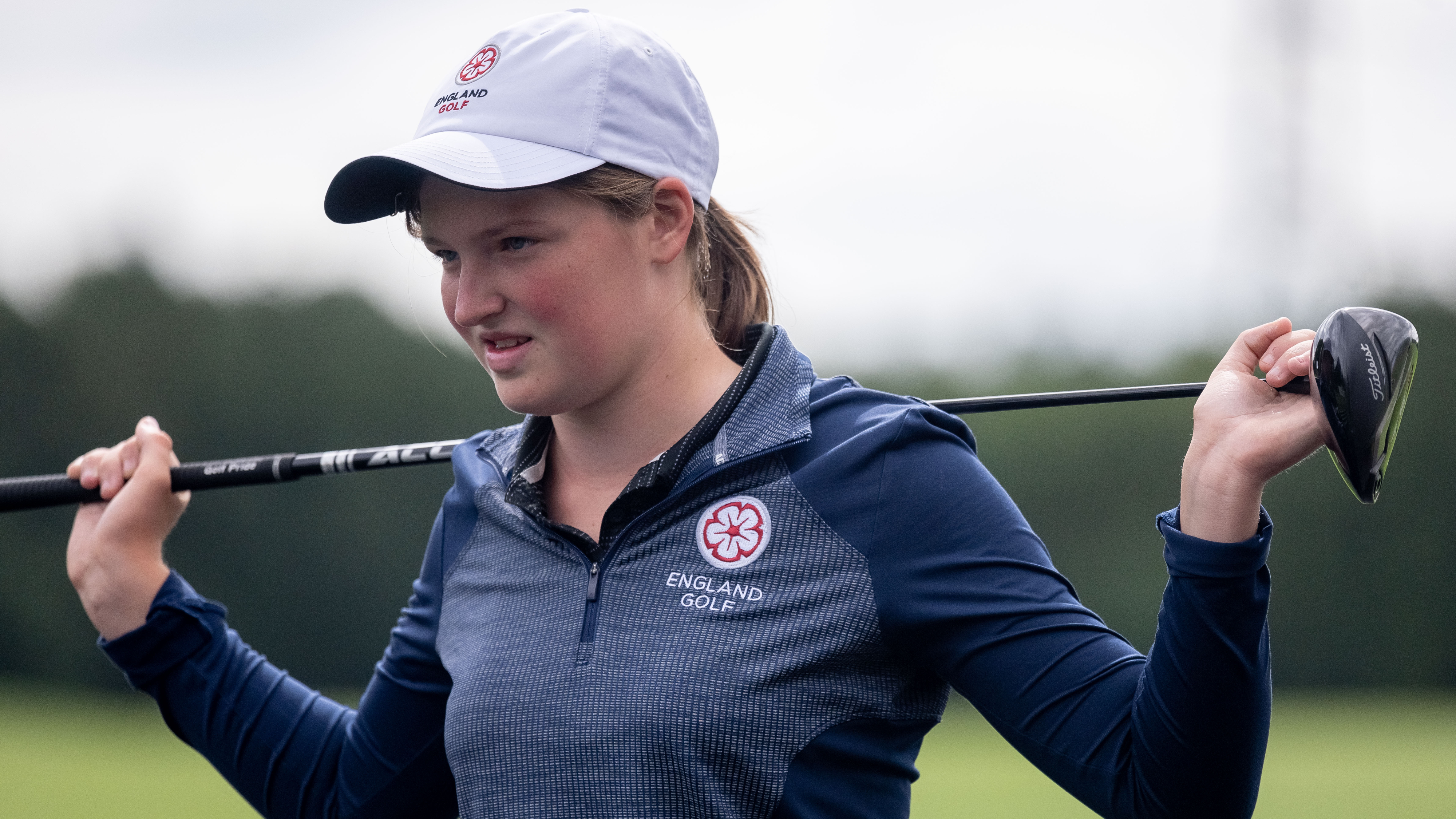 Lottie Woad holding her driver behind her back, wearing an England Golf top and cap