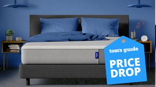 The Casper Mattress shown on a grey bed frame in a blue bedroom, with a blue price drop mattress sale badge overlaid on the image