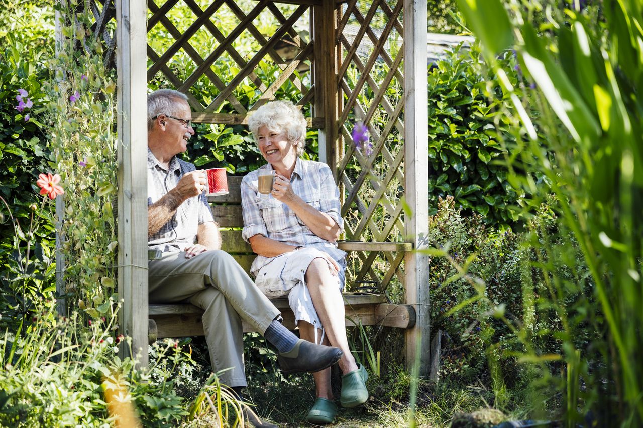 Retired couple sit on bench among plants in garden