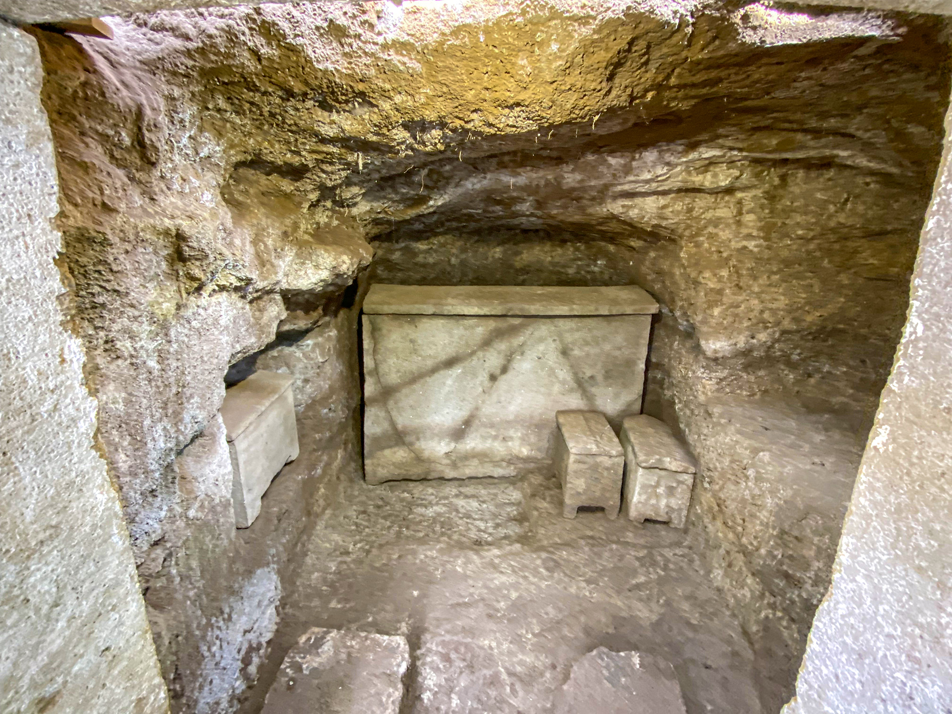 A stone sarcophagus in the center of the roman tomb along with three urns.