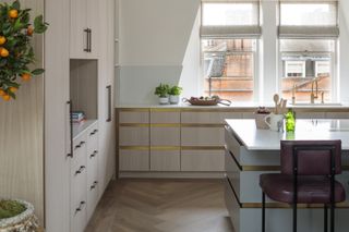 neutral and pale blue kitchen with herringbone floor, bar stools, kitchen island, brass trim