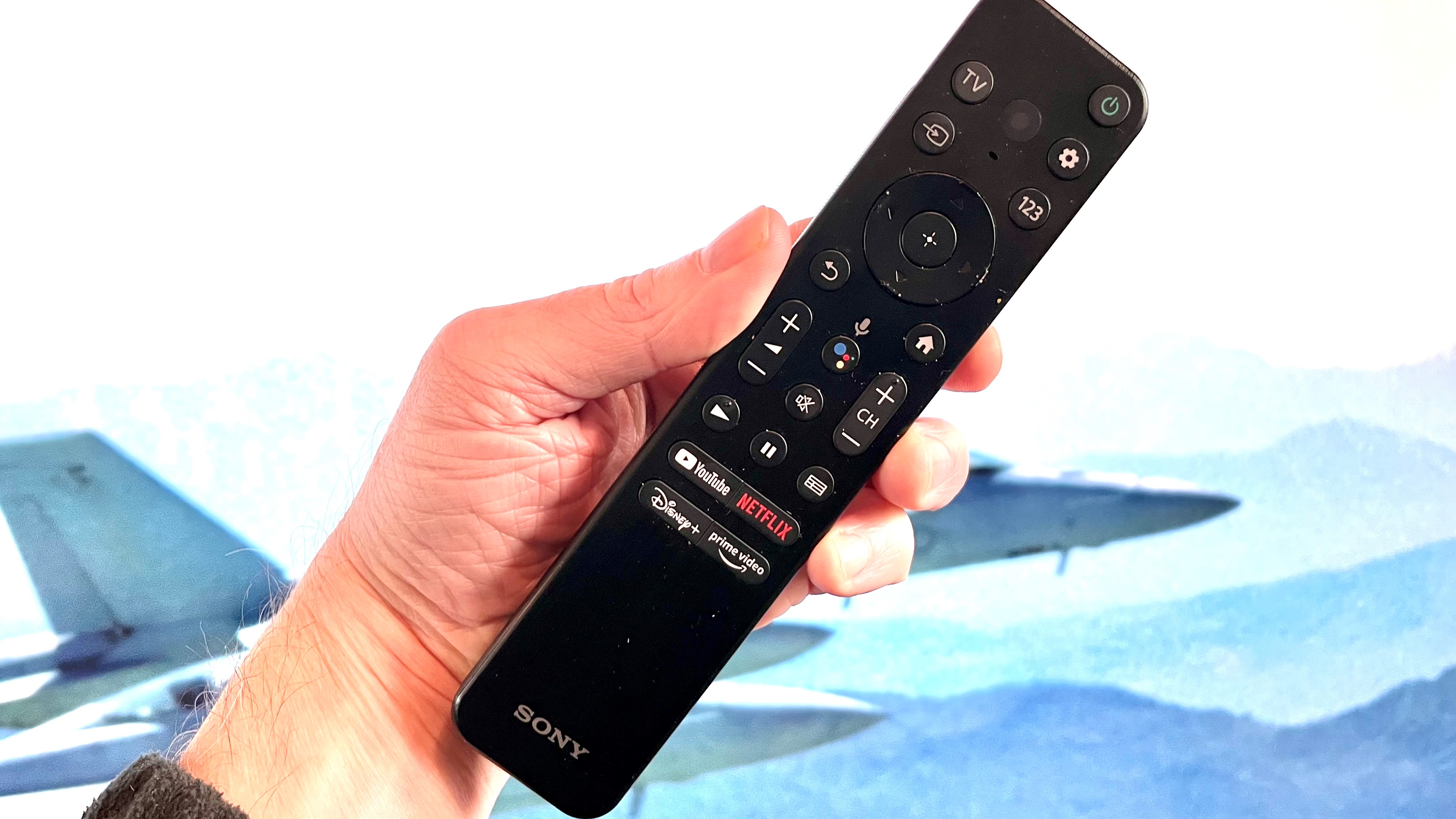 Sony X90K remote control held in hand with TV screen in background