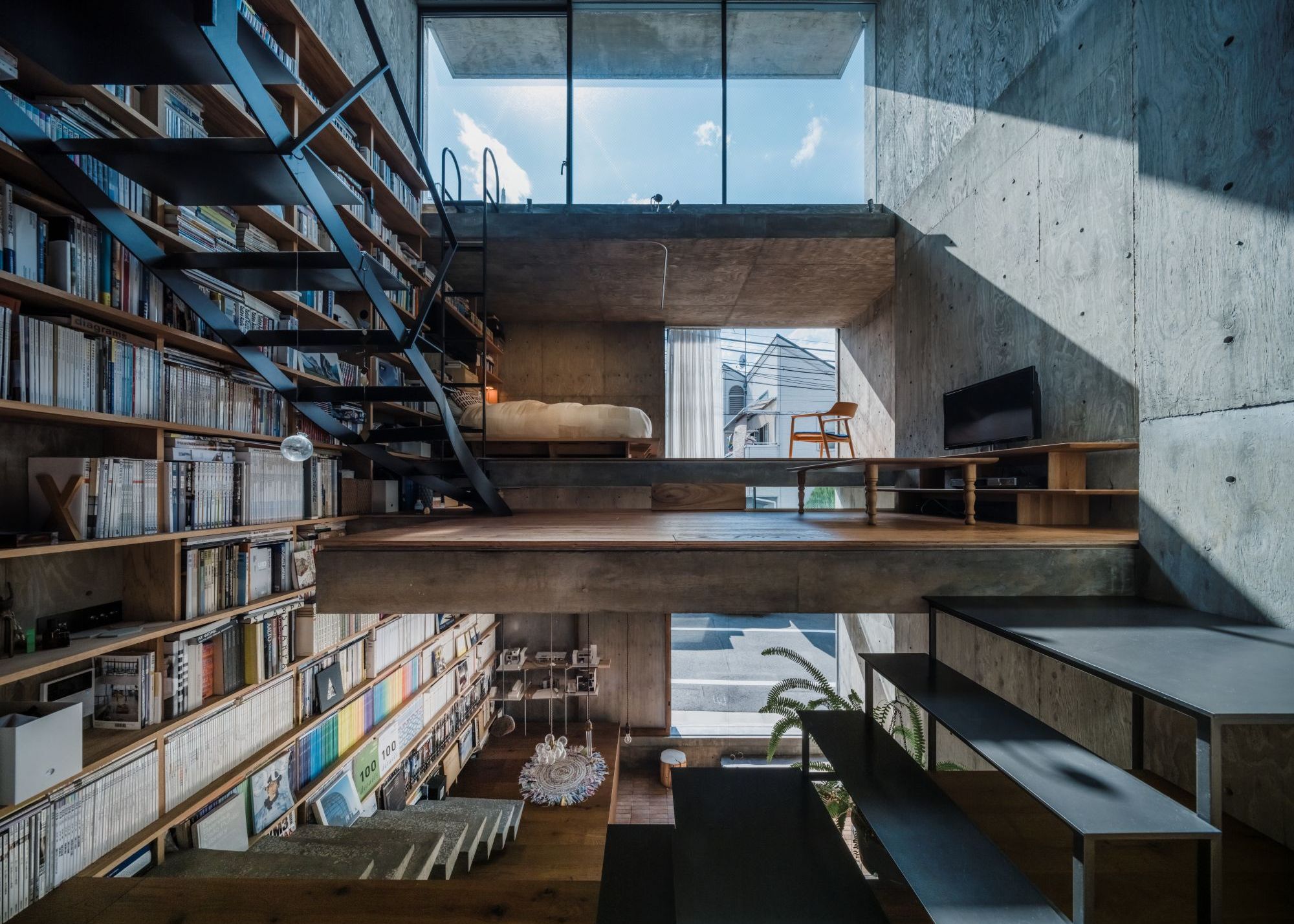 An open multi-layered Japanese home with concrete walls and ceiling, a bookcase that takes up the entire wall on one side, three stories up, with floating stairs and rooms with no doors