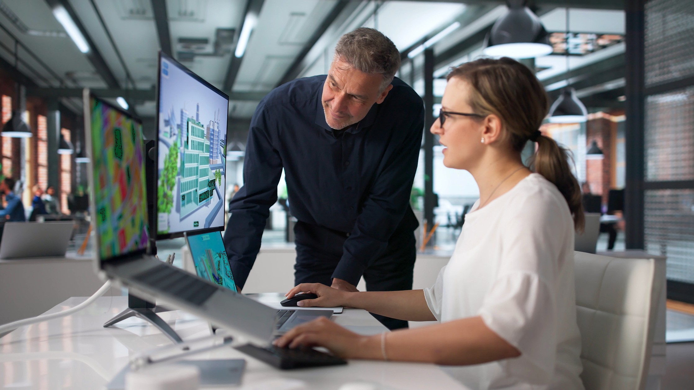 BIM Manager And Team Review 3D City Model Using Laptop Software. An older business owner looks at a monitor with a younger worker in a modern office.