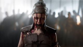 Senua stands staring at the camera, face covered in blood. An army holding torches can be seen, blurred, in the background behind her