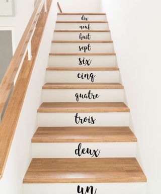 A white staircase with black staircase sticker decals with numbers written in French in serif-style typography