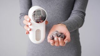 Someone holding a fabric shaver showing how much lint was removed from their gray knitwear