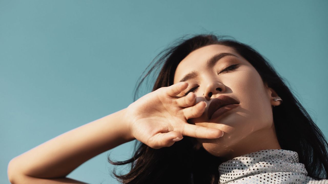 maybelline foundations - woman with eyes closed and hand to her face with blue sky behind her - gettyimages 1282563380