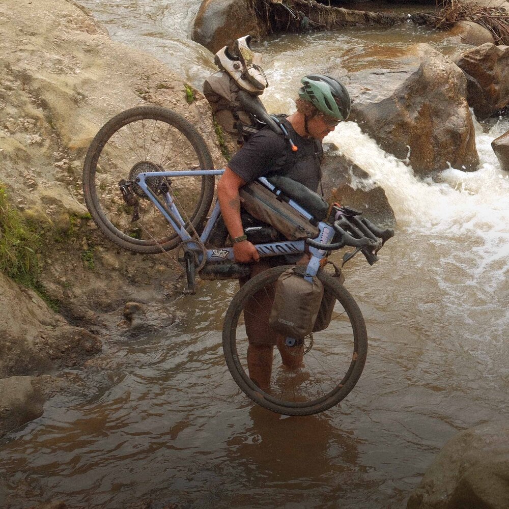 A rider carrying a Canyon Grizl across a stream