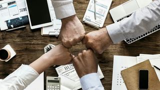 People fist bumping at the office - post-merger IT integration