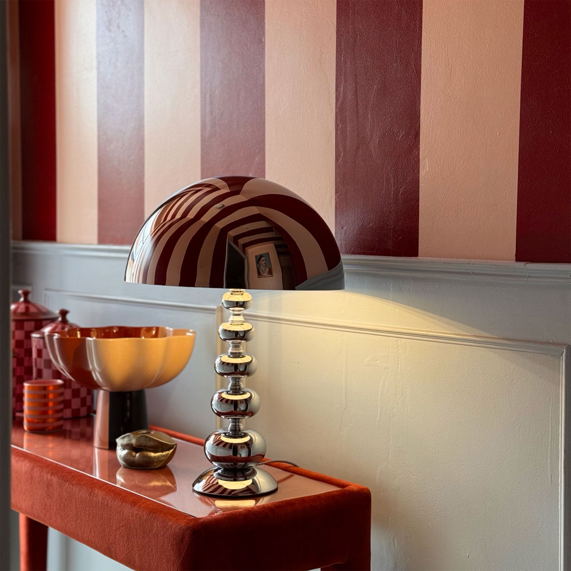 Chrome lamp on sideboard in front of pale blue wall topped with red stripes