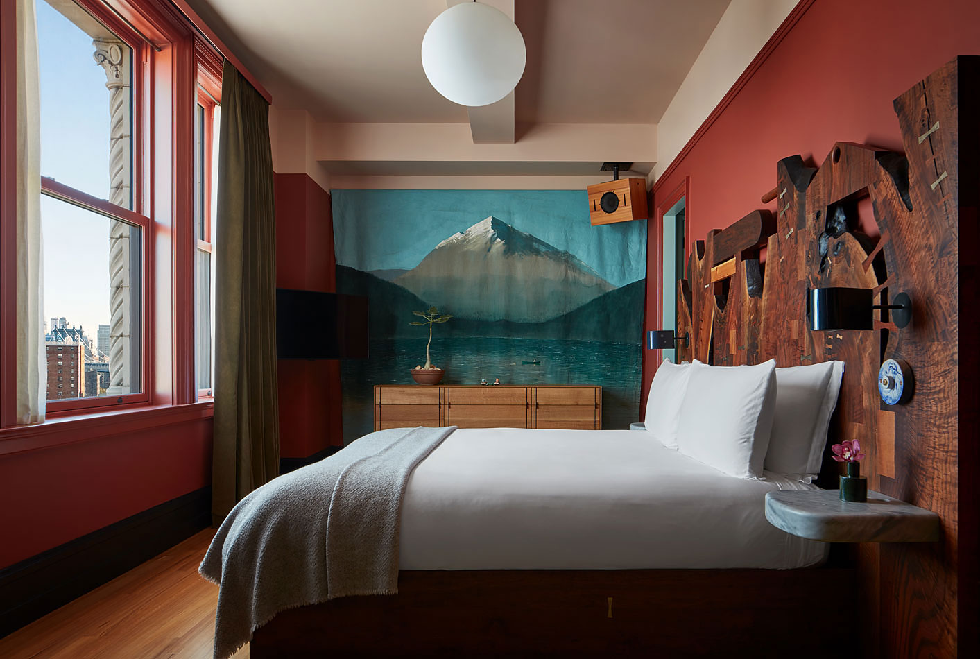 A modern glamour New York hotel boasts spherical Art Deco lighting paired with ornate walls filled with artworks and wooden cabinetry, all infused with soft pastels.