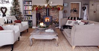 A neutral living room with a sofa facing two armchairs in front of a log burner with a Christmas tree to show how to decorate a living room for Christmas on a budget