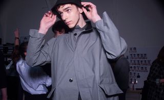 A model in a grey coat and bucket hat looking away in a dark room