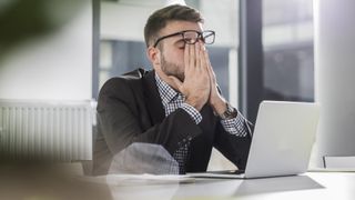 Exhausted young man with laptop in office