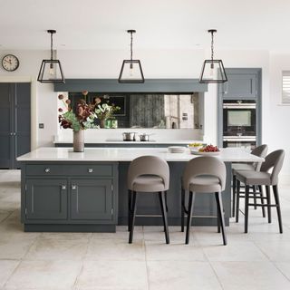 dark grey kitchen island with white worktop, grey stools, pendant lighting, grey cabinets and white walls