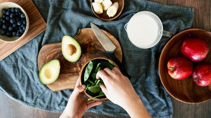 smoothie recipe ingredients flat lay on a table with avocado, apples, berries and bananas in bowls