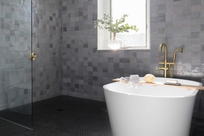 A bathroom with dark-toned wall tiles and white bathtub