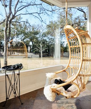 rattan chair hanging in window overlooking backyard with white dining table
