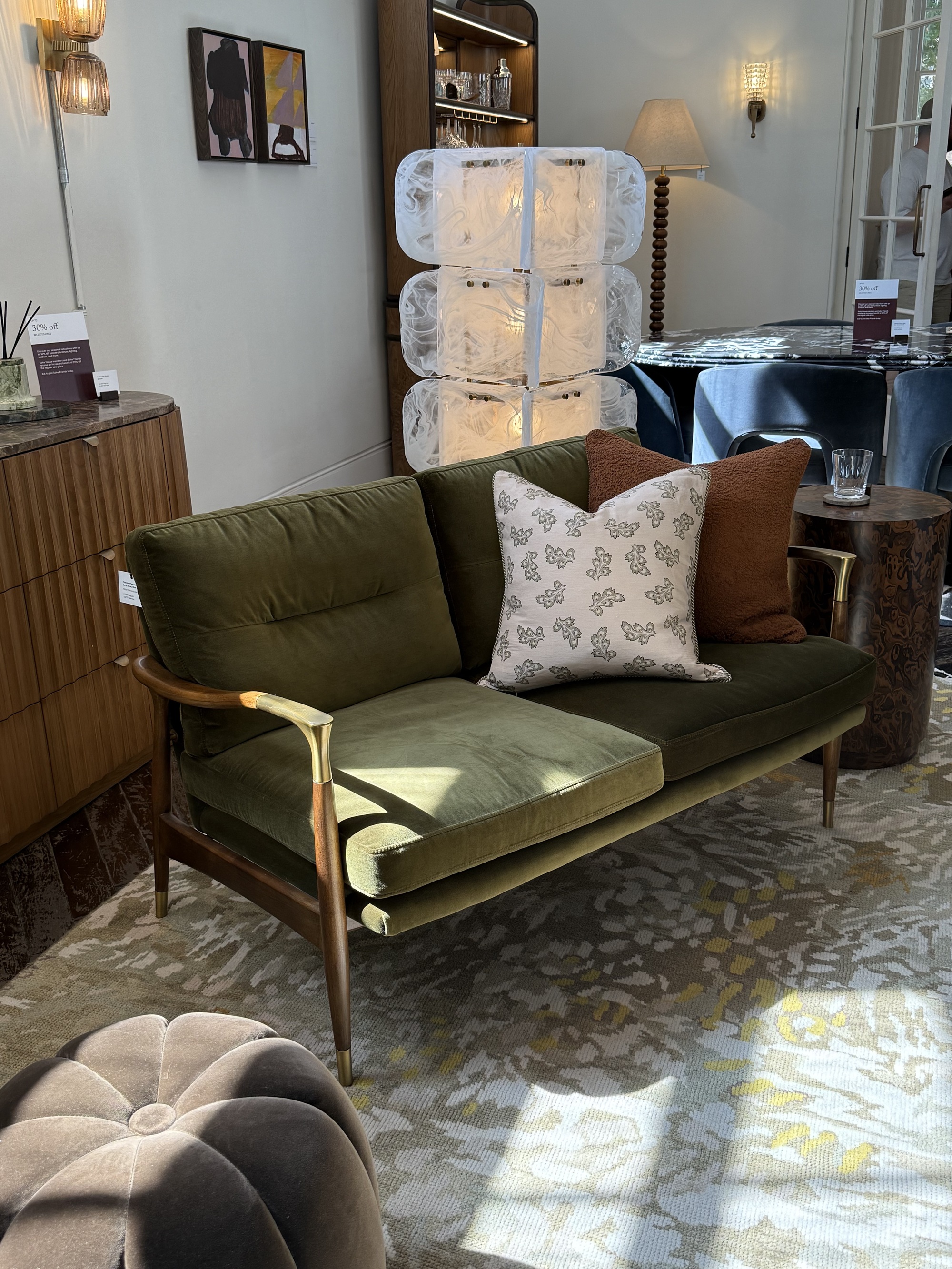 green mid-century style sofa with timber frame in soho home showroom in front of glass floor lamp, on patterned rug and styled with two cushions