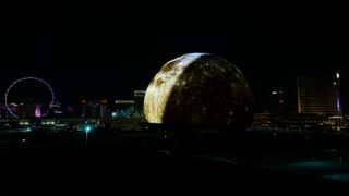 a giant spherical LED screen lit up to look like the moon, Mars and Earth