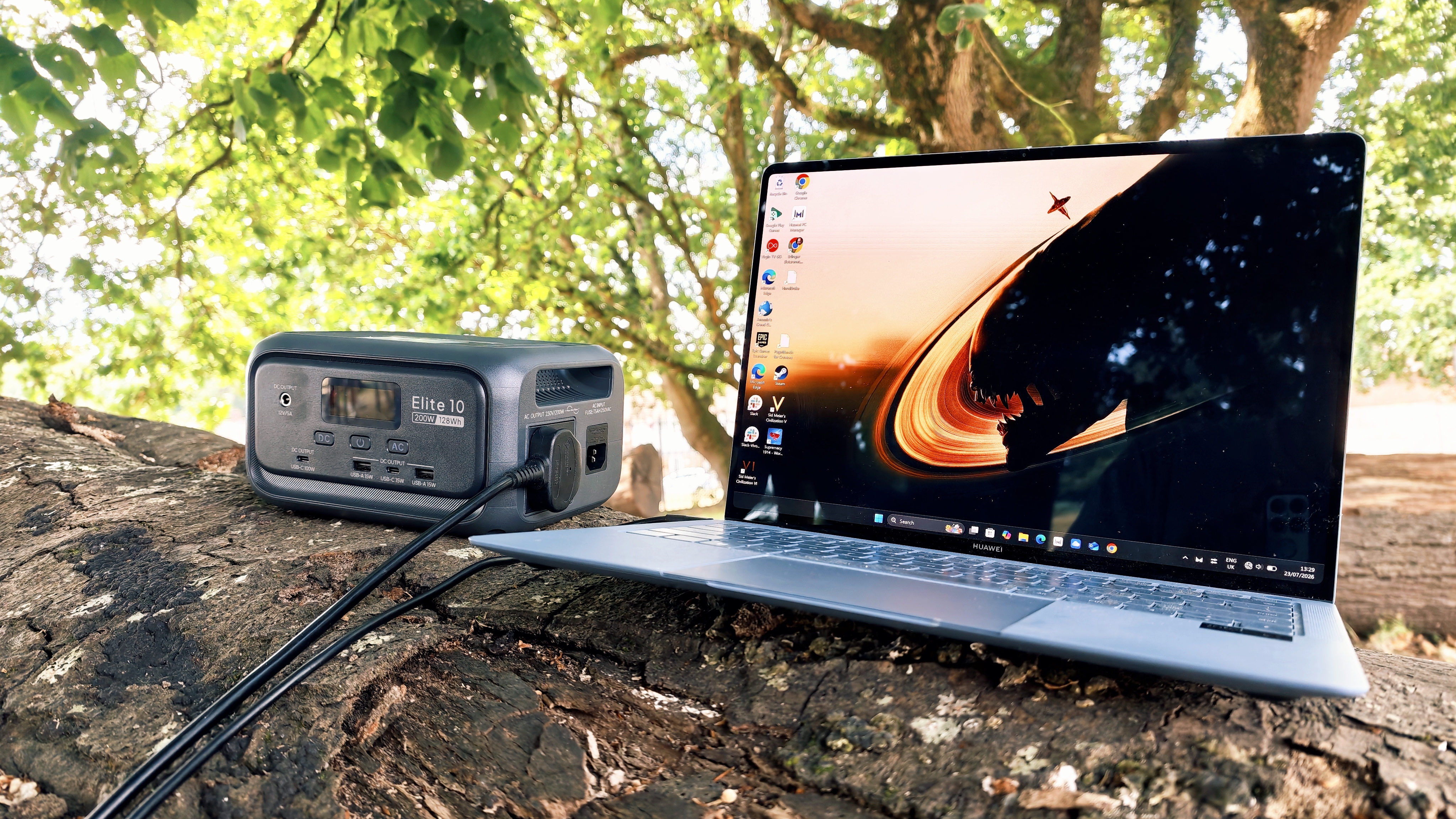 A grey Bluetti Elite 10 power station sitting on a log in a forest grove
