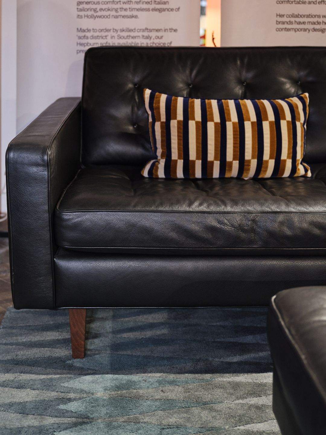 Front view of the Heal&rsquo;s Hepburn sofa in black leather, with slim arms, buttoned upholstery and tapered wooden legs.