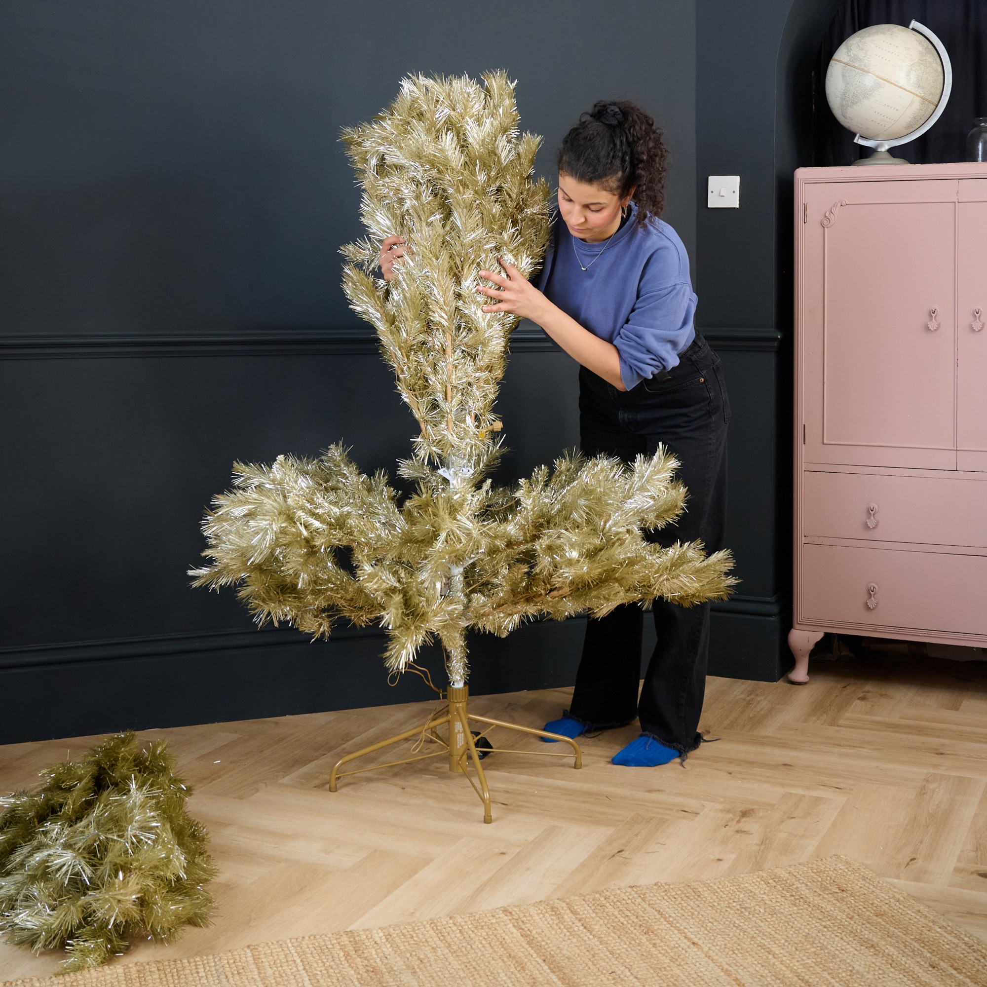 Sara putting together a John Lewis gold Christmas tree in a black-painted living room
