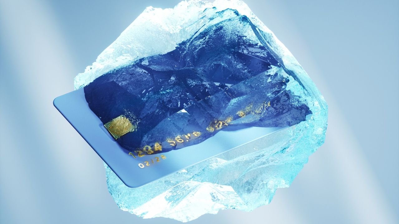 Credit card frozen in a block of ice against a light blue background