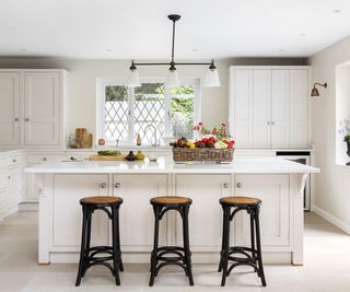 white kitchen with island unit and three black and wooden stools
