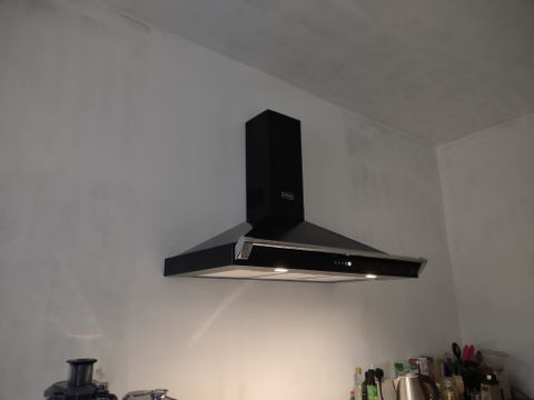A black pyramid chimney cooker hood fixed to a white kitchen wall