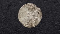 An ancient silver coin with stamp that depicts a seated Jesus.