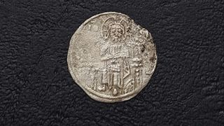 An ancient silver coin with stamp that depicts a seated Jesus.