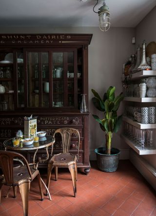 A vintage-inspired kitchen with red terracotta floor tiles, reclaimed metal table and chairs and large antique cabinet.