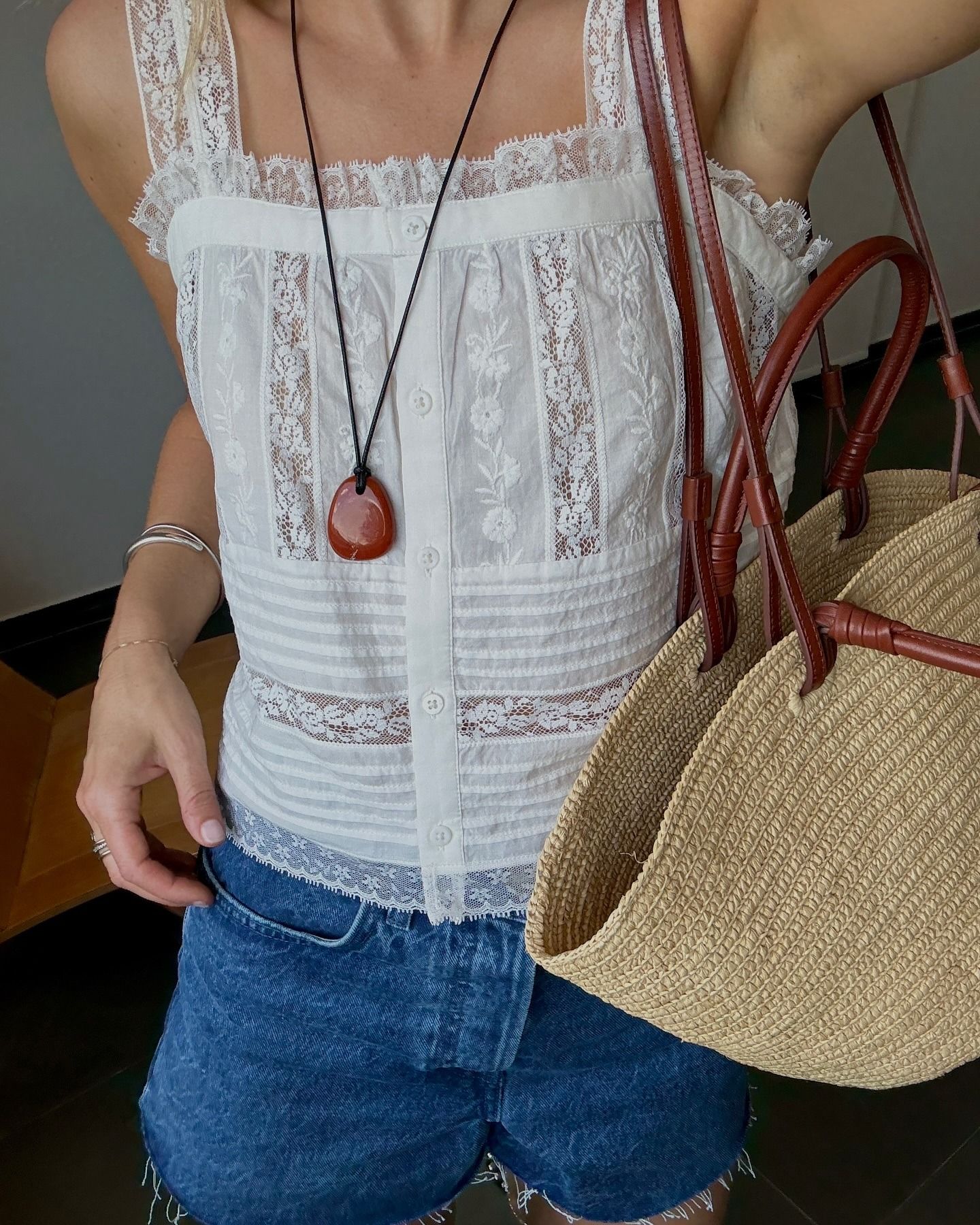 Close-up shot of influencer @lucywilliams02 wearing a white square-neck blouse from Sezane with cut-off denim, a large basket bag and a long pendant necklace.