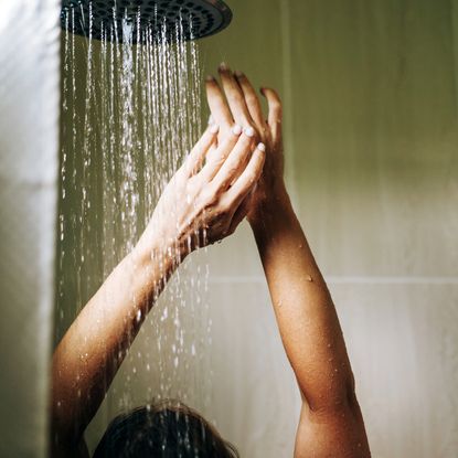 best shower oils - woman stretching arms up in the shower beneath falling water