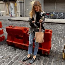 Courtney Grow wears jeans, black loafers and leather jacket, grey sweater and The Row bucket bag in New York. 