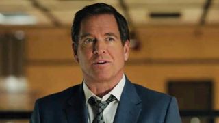 Michael Weatherly with the orange walls in the background in the NCIS Season 24 premiere. He has on a blue suit and tie.
