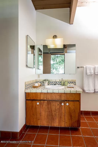 A dated bathroom with a wooden vanity with a tiled countertop