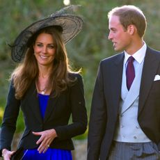 Kate Middleton wears a royal blue dress and a black jacket and hat while attending a wedding with Prince William in October 2010