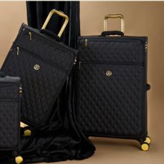 Black quilted IT Luggage suitcases with gold handles, beige background.